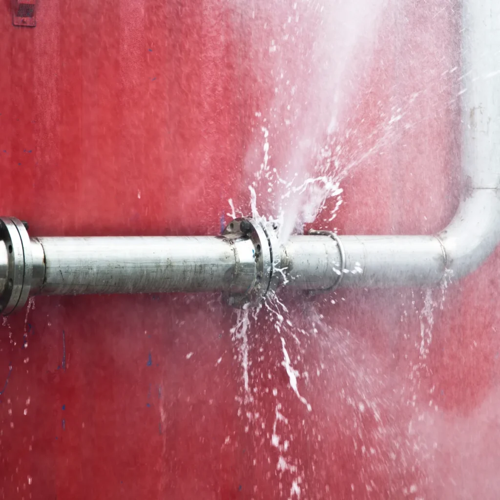 Water spraying from a damaged pipe joint against a red wall